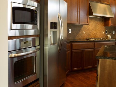 A kitchen with a built-in wall oven, a microwave and a stainless refrigerator fitted into dark wood cabinets.
