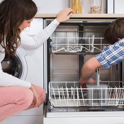 An open dishwasher with both racks drawn out while the installer works inside the tub.