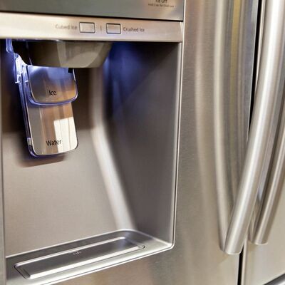 The ice and water dispenser set into the door of a stainless refrigerator.